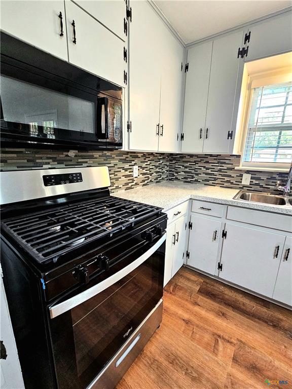 kitchen featuring decorative backsplash, wood finished floors, black microwave, light countertops, and stainless steel range with gas stovetop