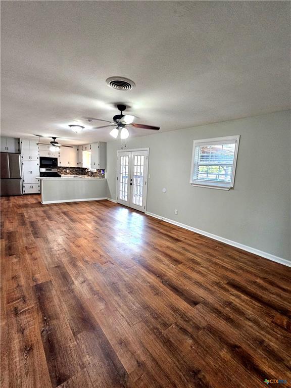 unfurnished living room featuring a textured ceiling, a ceiling fan, baseboards, visible vents, and dark wood-style floors