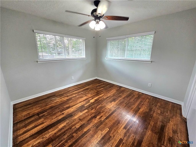 empty room featuring baseboards, plenty of natural light, dark wood-style floors, and ceiling fan