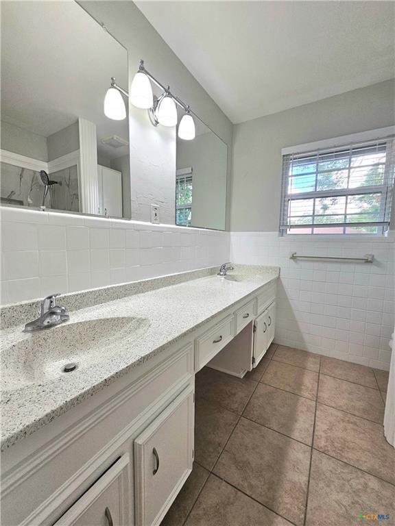 full bath with double vanity, tile walls, tile patterned flooring, walk in shower, and a sink