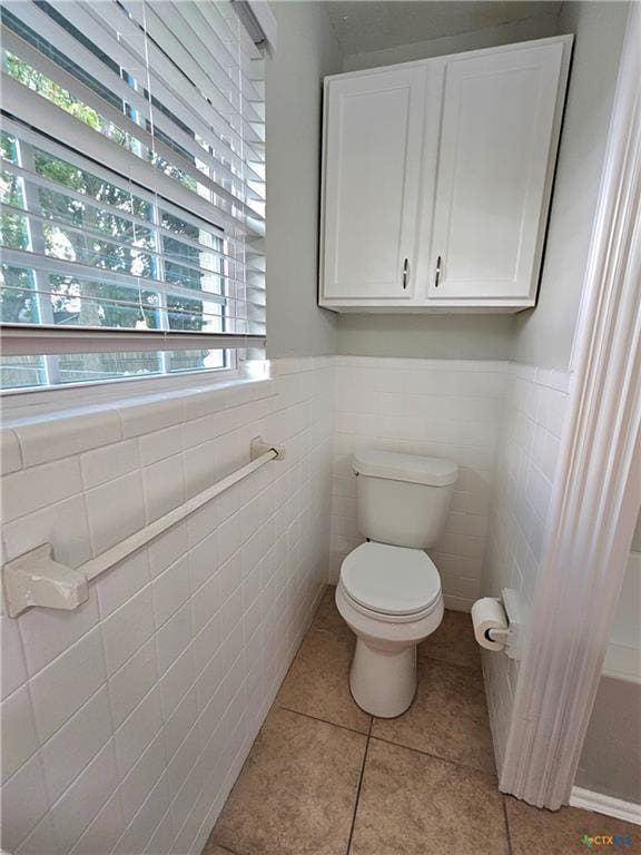 bathroom featuring tile patterned flooring, wainscoting, toilet, and tile walls