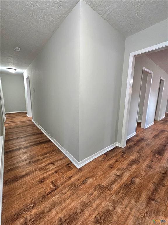 hall featuring baseboards, a textured ceiling, and wood finished floors