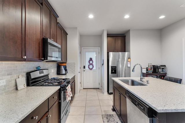 kitchen featuring light stone countertops, tasteful backsplash, stainless steel appliances, a kitchen island with sink, and sink