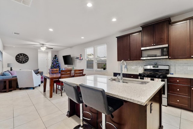 kitchen with light stone countertops, stainless steel appliances, ceiling fan, sink, and an island with sink