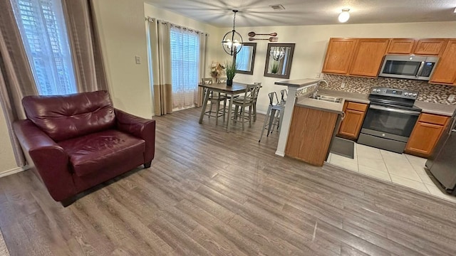 kitchen featuring stainless steel appliances, light hardwood / wood-style flooring, a notable chandelier, backsplash, and pendant lighting