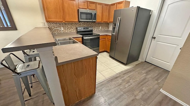 kitchen featuring kitchen peninsula, appliances with stainless steel finishes, light wood-type flooring, a breakfast bar, and sink