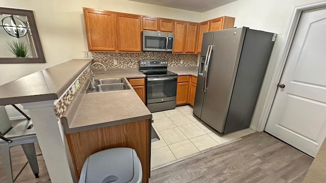 kitchen with light wood-type flooring, tasteful backsplash, stainless steel appliances, sink, and decorative light fixtures