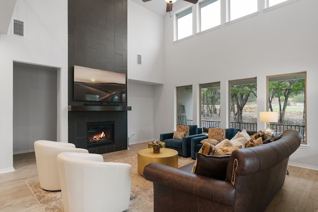 living room featuring a tile fireplace, a high ceiling, light wood-type flooring, and ceiling fan