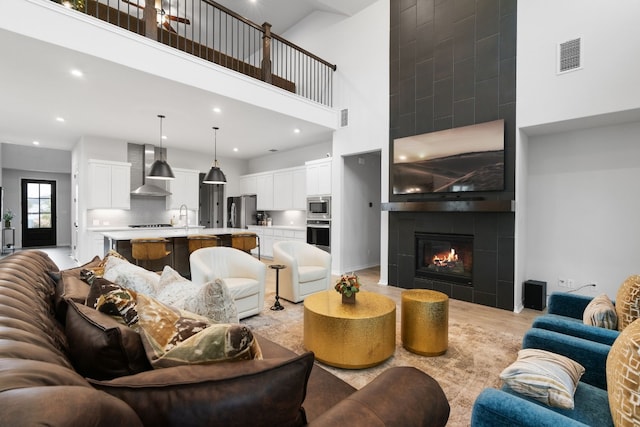 living room featuring light hardwood / wood-style flooring, a high ceiling, and a tiled fireplace