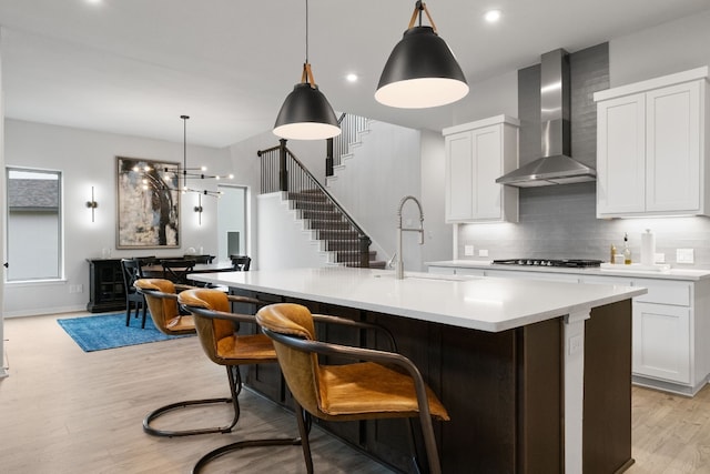 kitchen with wall chimney exhaust hood, sink, decorative light fixtures, light hardwood / wood-style flooring, and white cabinets