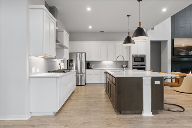 kitchen featuring sink, an island with sink, pendant lighting, appliances with stainless steel finishes, and light wood-type flooring