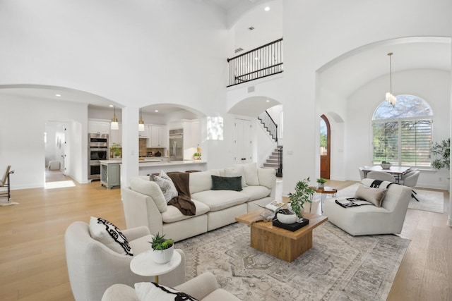 living room featuring stairway, baseboards, a high ceiling, recessed lighting, and light wood-type flooring