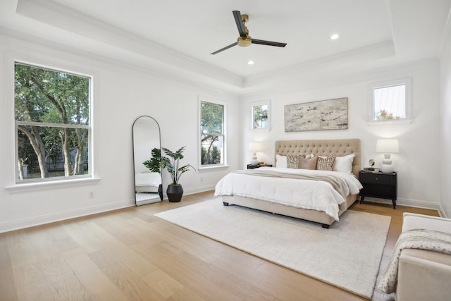 bedroom featuring light wood-type flooring, ceiling fan, ornamental molding, and a tray ceiling