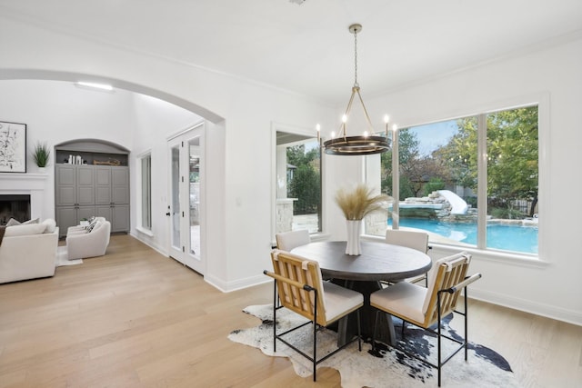 dining room with a notable chandelier, arched walkways, a fireplace, light wood finished floors, and baseboards