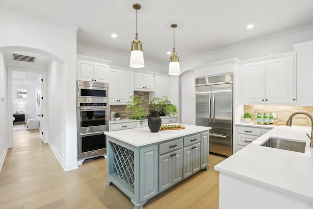 kitchen featuring gray cabinetry, a center island, arched walkways, stainless steel appliances, and a sink