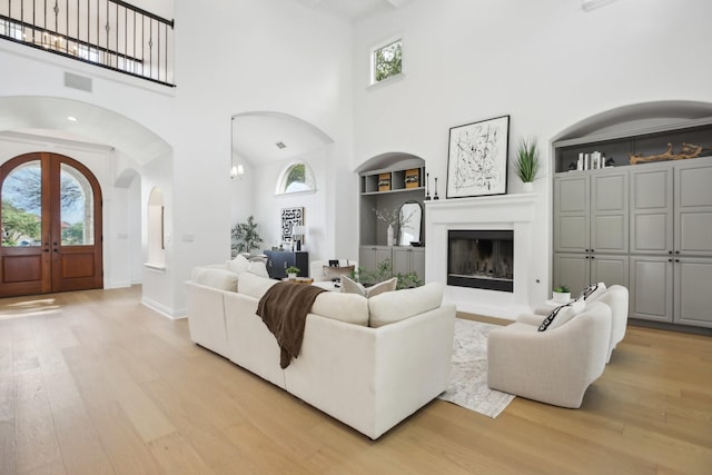 living room featuring built in features, light wood-type flooring, and a towering ceiling