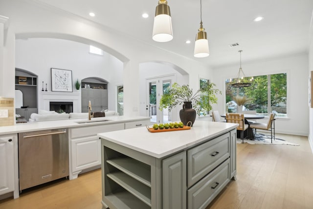 kitchen featuring white cabinetry, stainless steel dishwasher, sink, decorative light fixtures, and a kitchen island