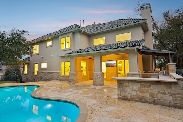 rear view of house with a fenced in pool, a tile roof, stucco siding, a chimney, and a patio area