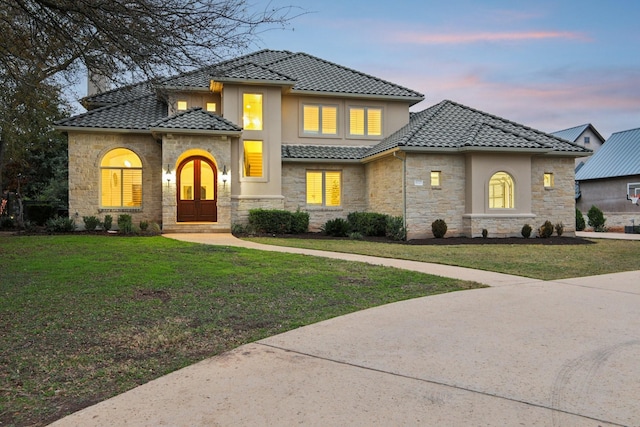 view of front facade featuring a yard, stone siding, stucco siding, and a tiled roof