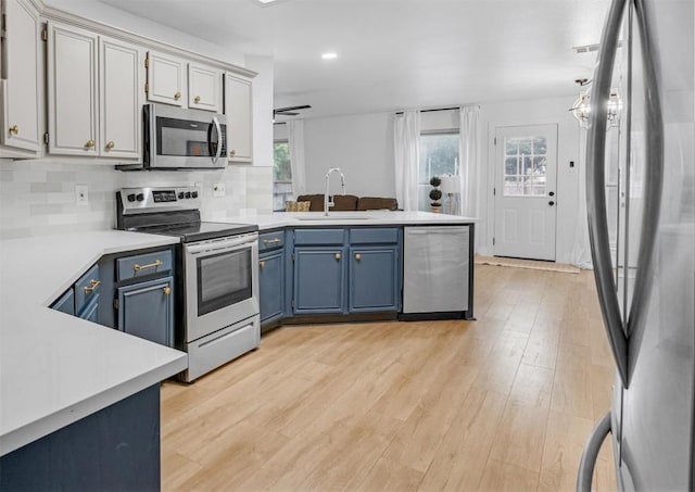 kitchen featuring sink, light hardwood / wood-style flooring, blue cabinets, decorative backsplash, and appliances with stainless steel finishes