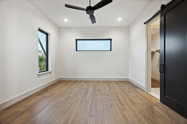 spare room with a barn door, light hardwood / wood-style floors, and ceiling fan