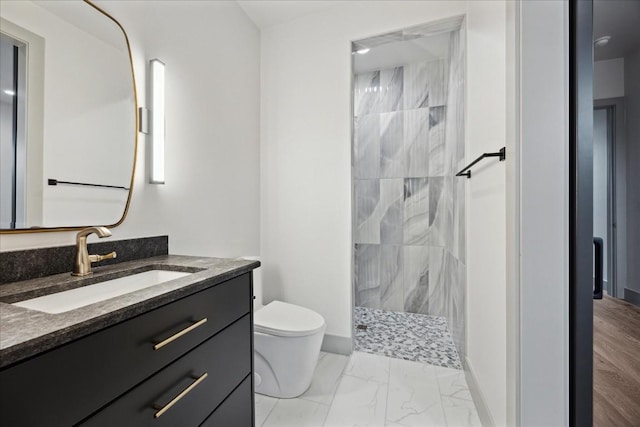 bathroom with a tile shower, vanity, and toilet