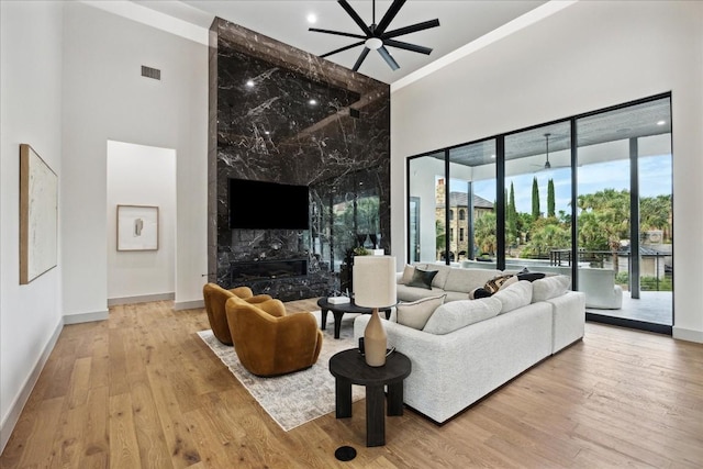 living room with a high ceiling, light wood-type flooring, ceiling fan, and a premium fireplace