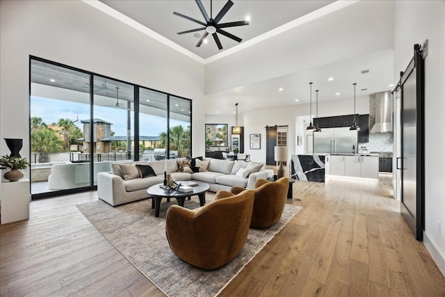 living room with ceiling fan, light hardwood / wood-style floors, a barn door, and a high ceiling