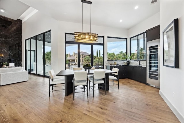 dining space featuring a chandelier, light wood-type flooring, beverage cooler, and sink