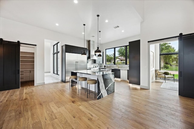 kitchen with a breakfast bar, a kitchen island with sink, built in fridge, a barn door, and light hardwood / wood-style floors