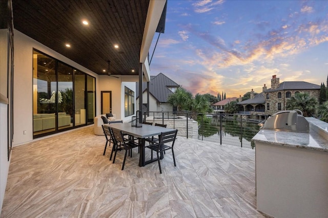 patio terrace at dusk featuring an outdoor kitchen, a water view, and area for grilling