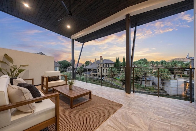 patio terrace at dusk with outdoor lounge area, ceiling fan, and a balcony