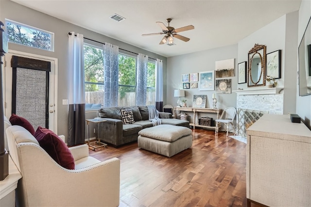 living room featuring visible vents, a ceiling fan, a fireplace with flush hearth, and wood finished floors