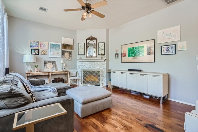 living room featuring a stone fireplace, ceiling fan, and dark wood-type flooring