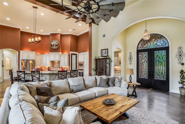 living room featuring french doors, ceiling fan with notable chandelier, a high ceiling, and ornamental molding