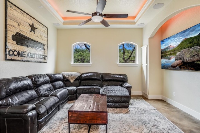 living room featuring concrete flooring, a raised ceiling, ceiling fan, and ornamental molding