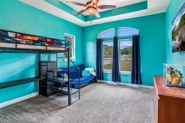 carpeted bedroom with ceiling fan and a tray ceiling