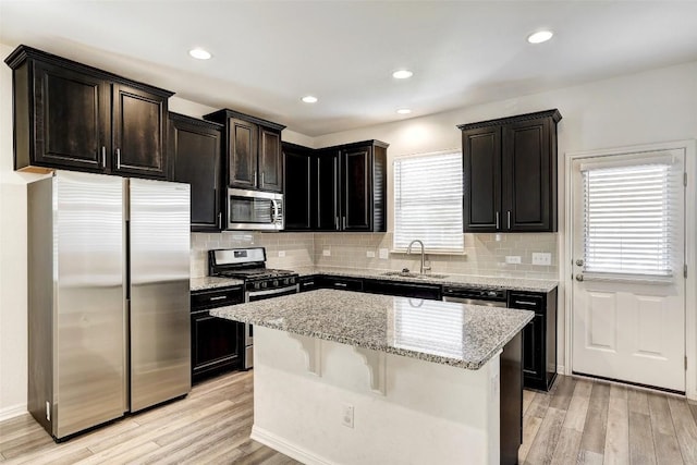 kitchen with stainless steel appliances, a center island, a sink, and light wood finished floors