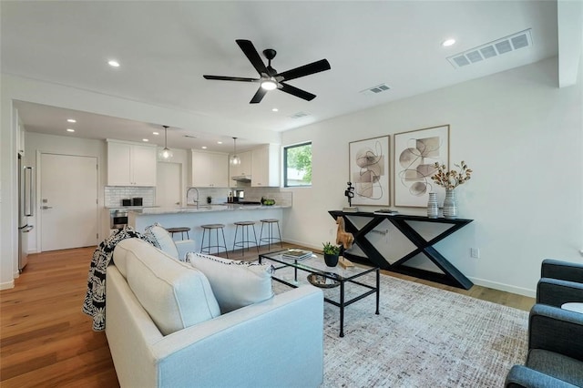 living room featuring ceiling fan, sink, and light wood-type flooring