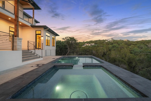 pool at dusk with an in ground hot tub