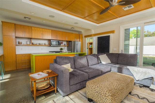 living room featuring ceiling fan, sink, a tray ceiling, and concrete floors