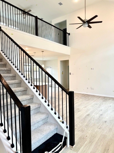 stairway with wood-type flooring, a towering ceiling, and ceiling fan