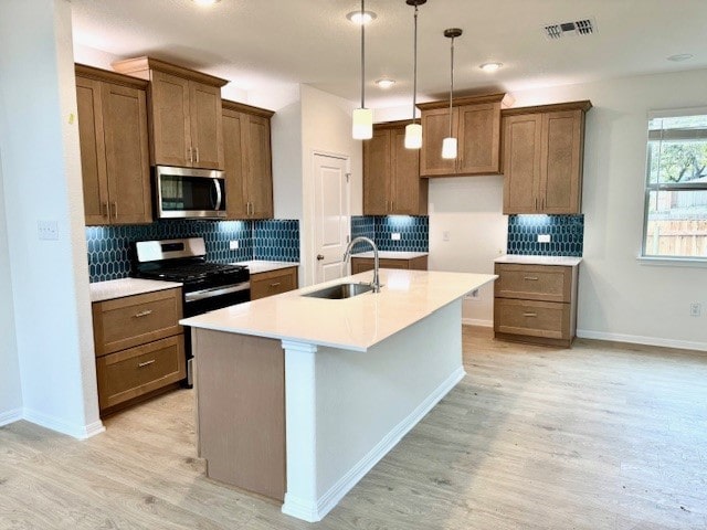 kitchen featuring sink, pendant lighting, a center island with sink, appliances with stainless steel finishes, and light wood-type flooring