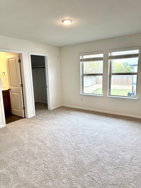 unfurnished bedroom featuring a walk in closet, a textured ceiling, connected bathroom, carpet floors, and a closet