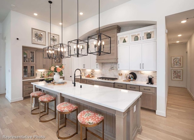 kitchen featuring a large island with sink, white cabinetry, light hardwood / wood-style flooring, and pendant lighting