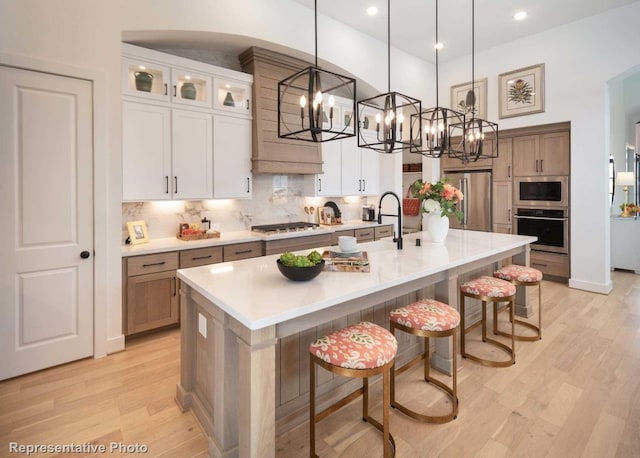 kitchen featuring a large island with sink, white cabinets, light hardwood / wood-style flooring, appliances with stainless steel finishes, and decorative light fixtures