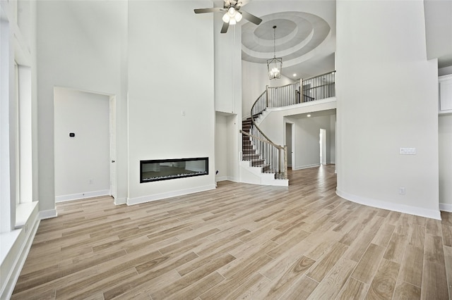 149 Golden Sage Ave, Georgetown, TX 78633 - unfurnished living room with a towering ceiling, stairs, light wood-style flooring, a glass covered fireplace, and a ceiling fan