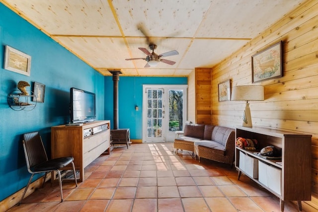 living area with ceiling fan, light tile patterned floors, a wood stove, and wooden walls