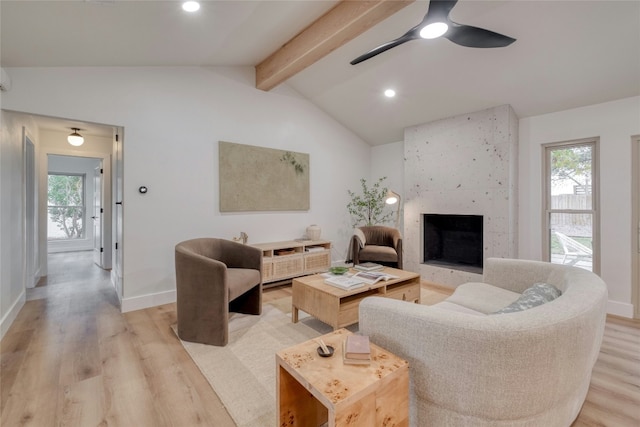 living room featuring a large fireplace, lofted ceiling with beams, light hardwood / wood-style floors, and ceiling fan