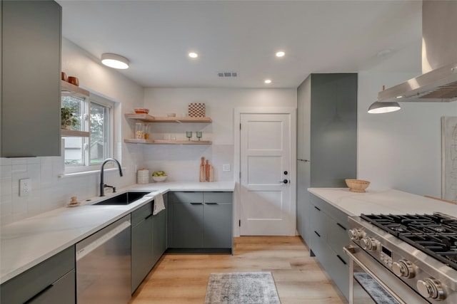 kitchen featuring sink, wall chimney exhaust hood, tasteful backsplash, appliances with stainless steel finishes, and light wood-type flooring